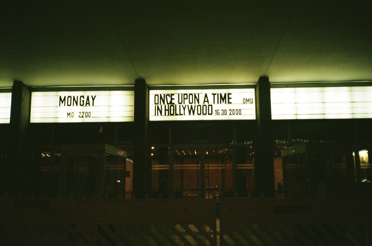 Outdoor view of an illuminated theater marquee displaying movie titles at night.